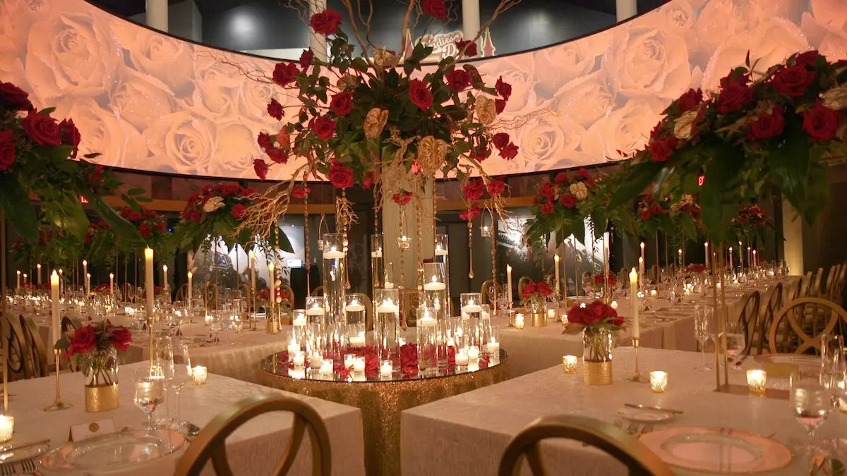 Elegant banquet table decorated with red roses, tall candles, and floating candles in glass vases under a circular floral backdrop.