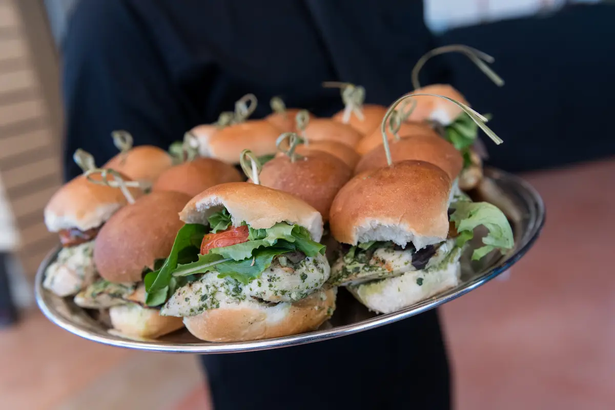 Tray full of chicken sandwiches with lettuce and tomato held by a server