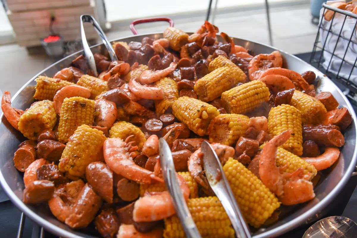 Large bowl filled with cooked shrimp, sliced sausage, and seasoned corn on the cob.